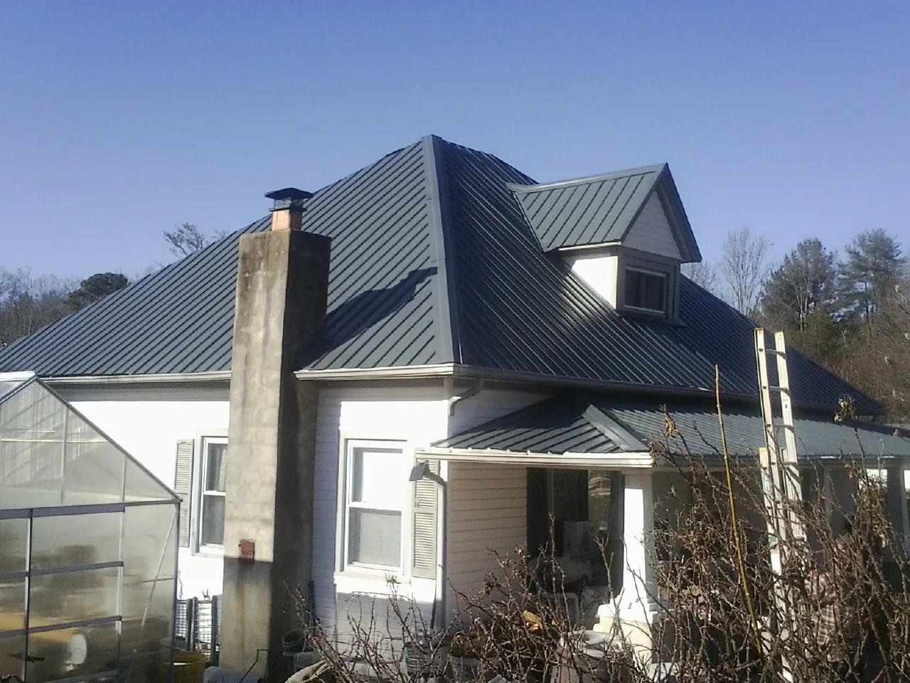 Dark blue standing seam metal roof on a white farmhouse with dormer — Slate & Tile Roof Repair by Roofing Brothers in Elko