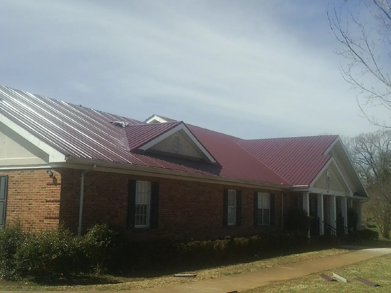 Red metal roof with gabled entries on a long brick building, from a Hail Damage Roof Repair job in Elko