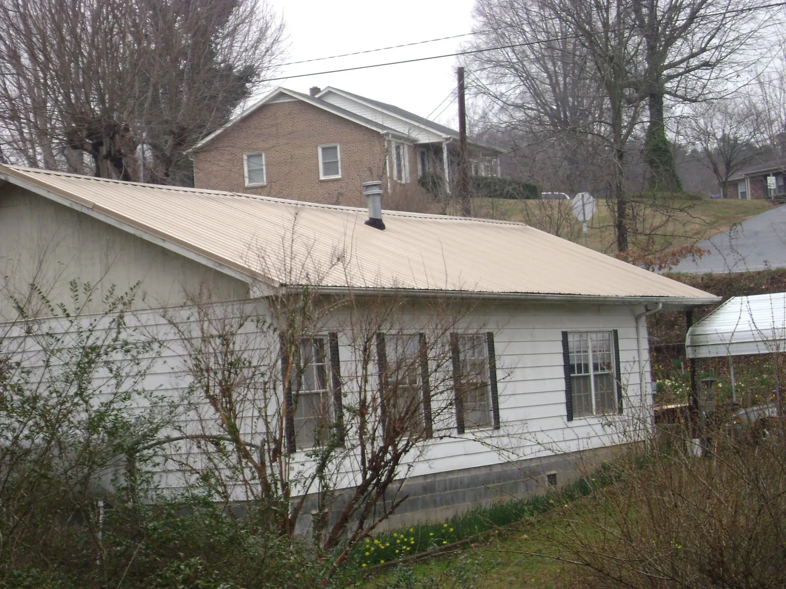 Tan metal roof on a white sided house set into a hillside — Commercial Roofing by Roofing Brothers in Elko